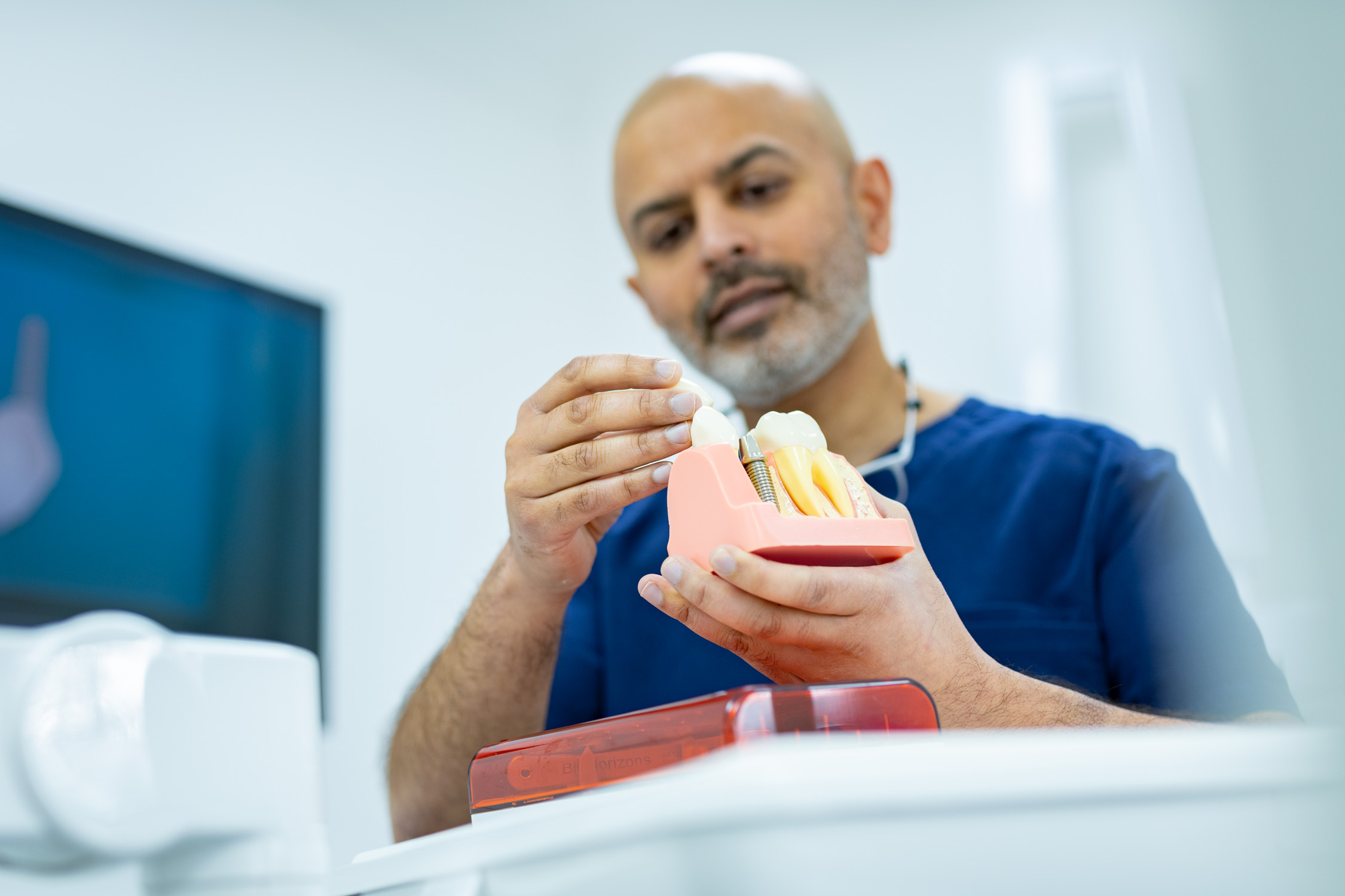 Dr Naresh Hirani holding a dental implant model